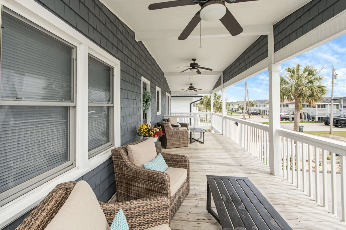 A welcoming back porch with comfortable seating, decorative plants, and wooden flooring. Ceiling fans offer a cool breeze, and the porch looks out onto a vibrant sunset sky, suggesting an inviting atmosphere for evening relaxation with friends.