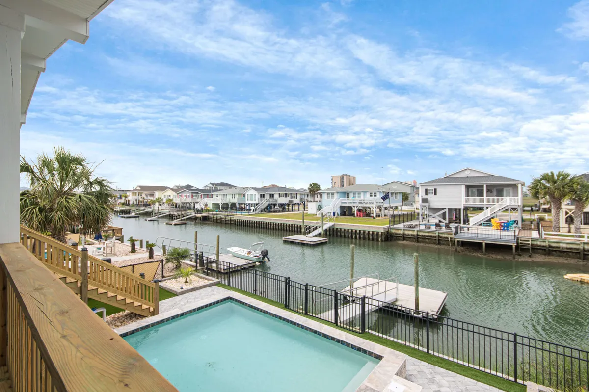 A vibrant poolside area overlooks a serene waterway, surrounded by palm trees and neighboring docks. The swimming pool is at the heart of the scene, ideal for gatherings. The setting is perfectly tailored for outdoor leisure, with space for sunbathing, barbecuing, and relaxing as boats pass by on the channel.