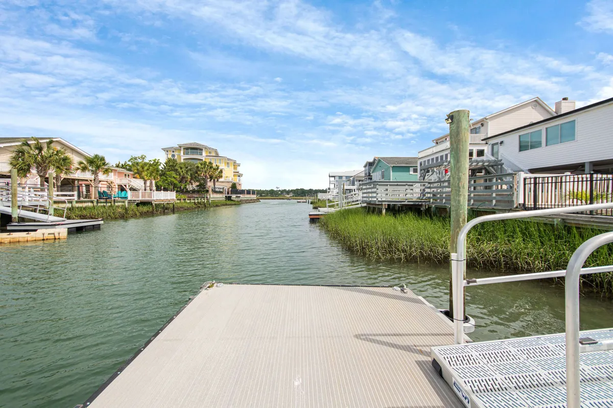 A tranquil dock scene featuring a peaceful waterway, surrounding houses, and lush vegetation. The dock offers a perfect launch point for kayaks or paddleboards, or a spot to enjoy coffee and nature as the sun sets over the water.