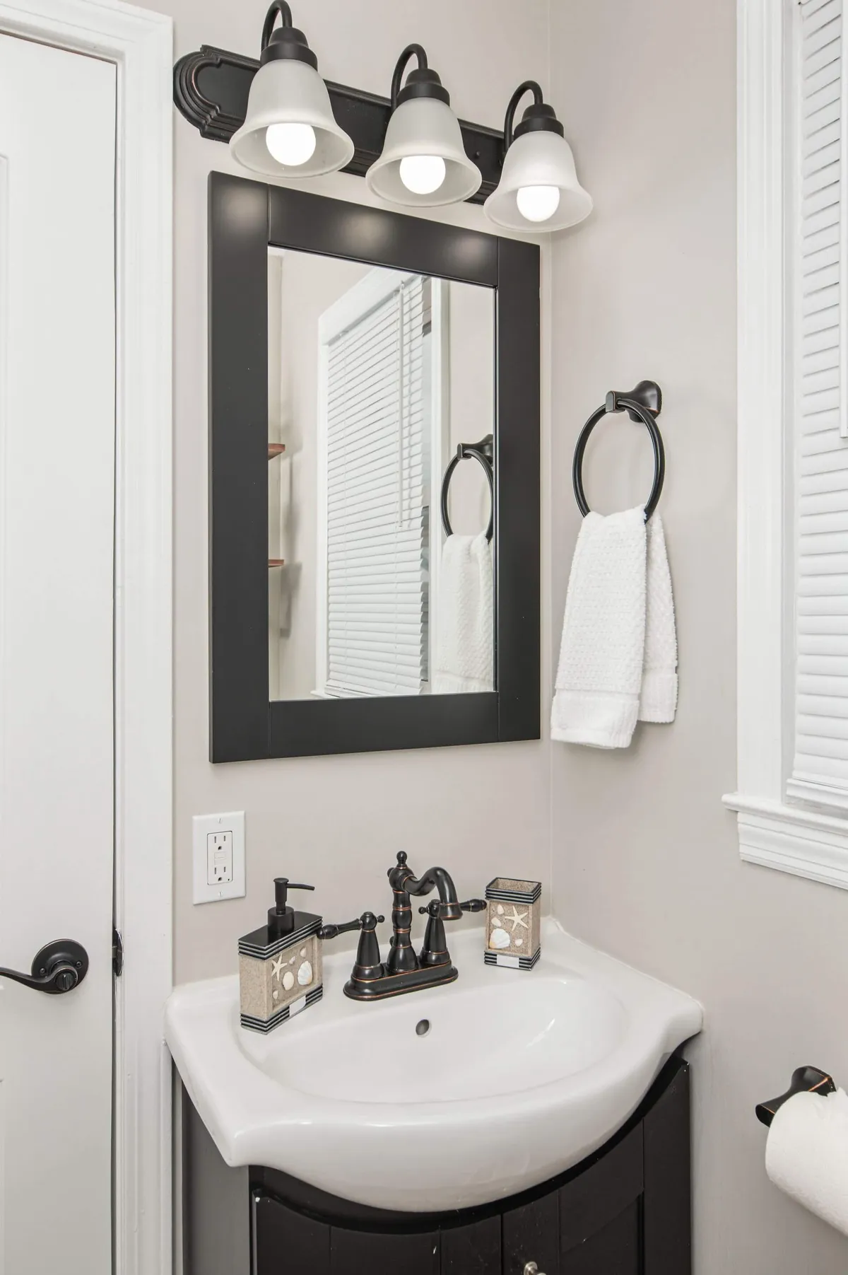 A modern bathroom with a stylish sink, a large mirror, well-placed light fixtures, fluffy towels, and carefully chosen decorative containers. The space feels both functional and welcoming, ideal for daily routines or quick refreshes.