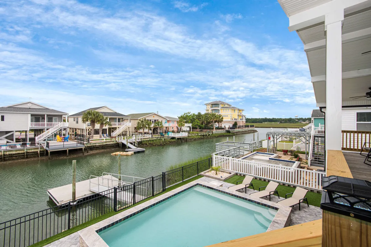 This exterior image features a sparkling swimming pool with the calm channel and surrounding houses visible in the background. Lounge chairs and a relaxing poolside setting create a welcoming space for both kids and adults. The view captures the vibrant energy of resort-style living, while the waterway hints at nearby fishing and boating activities.