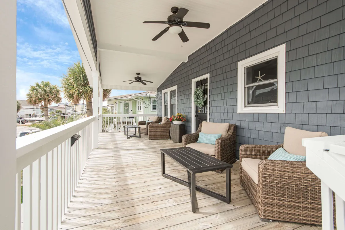 A welcoming porch scene with wicker seating and a coffee table, framed by palm trees and illuminated by soft natural light. The space is designed for relaxing, sharing drinks, and soaking in the peaceful ambiance, with sunrise or evening lighting suggesting a romantic atmosphere.