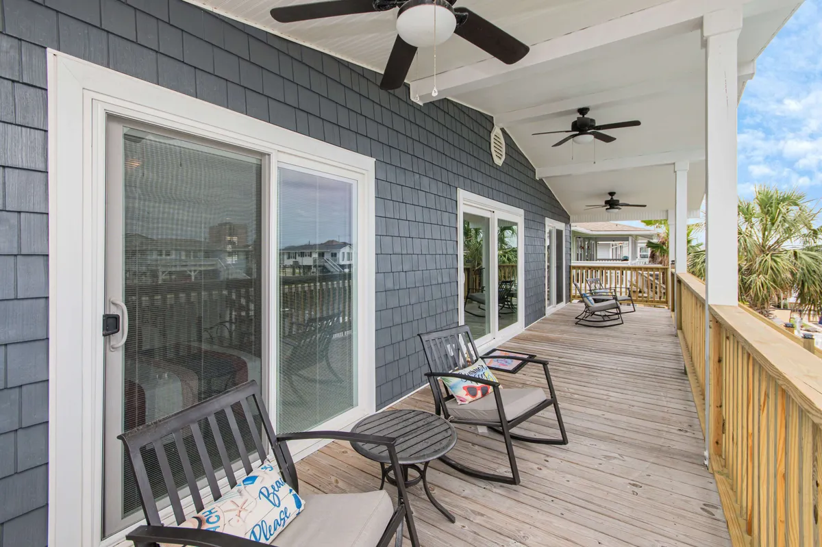 This image features a serene exterior deck setup with comfortable deck chairs facing a beautiful view of the surrounding waterway and landscape. Ceiling fans hang overhead, adding comfort, while the setting is perfect for enjoying a peaceful moment outdoors. The lighting suggests either sunrise or sunset, contributing to a calm and romantic mood.
